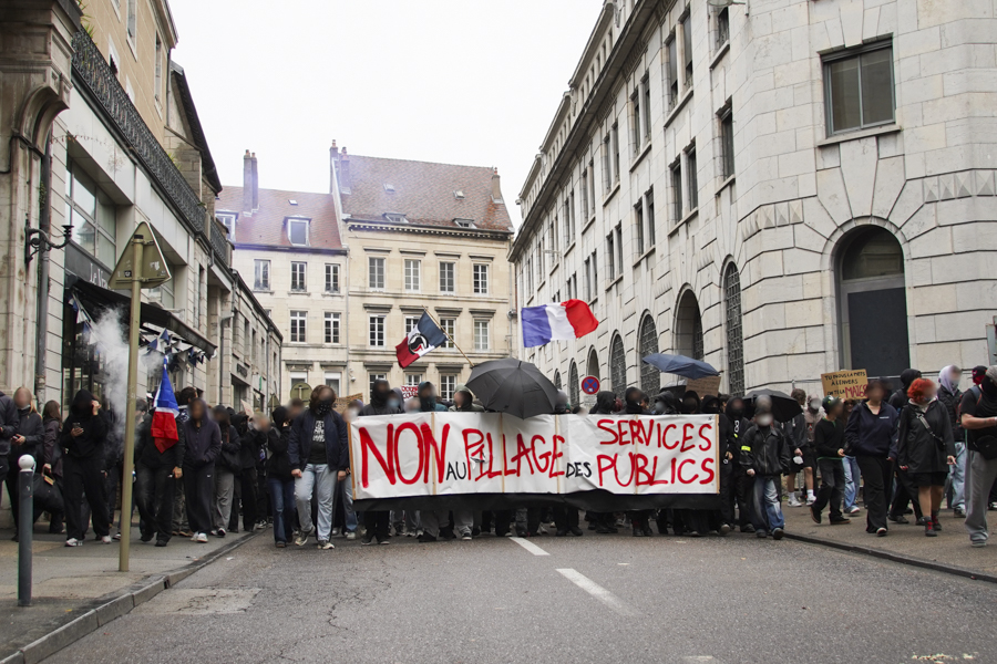 La tête de cortège dans la rue de la préfecture avec une banderole de tête portant l'inscription "non au pillage des services publiques" avec plusieurs drapeau bleu-blanc-rouge dont un portant l'inscription "action antifasciste"